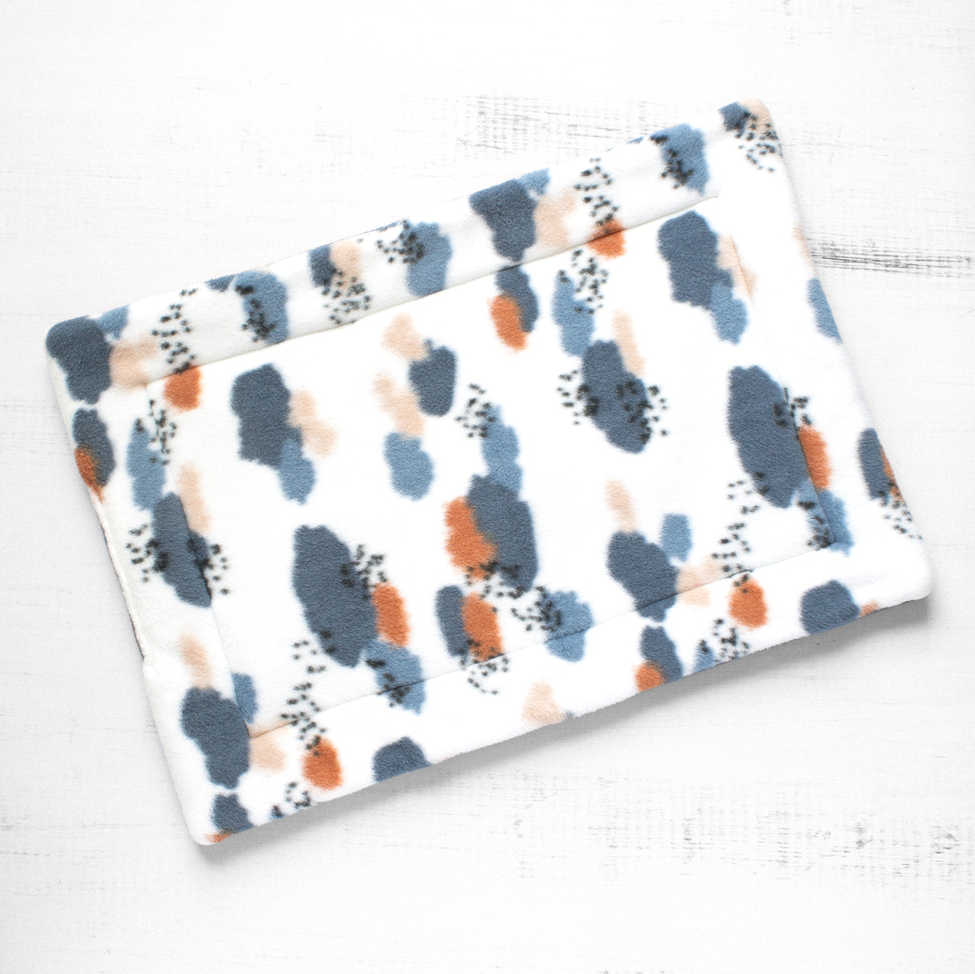 Top view of cat mat with abstract pattern of blues and oranges.