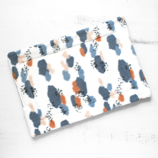 Top view of cat mat with abstract pattern of blues and oranges.