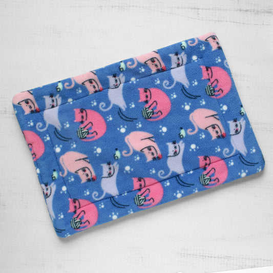 Top view of cat mat with pink and blue cats playing with toys on a blue background.