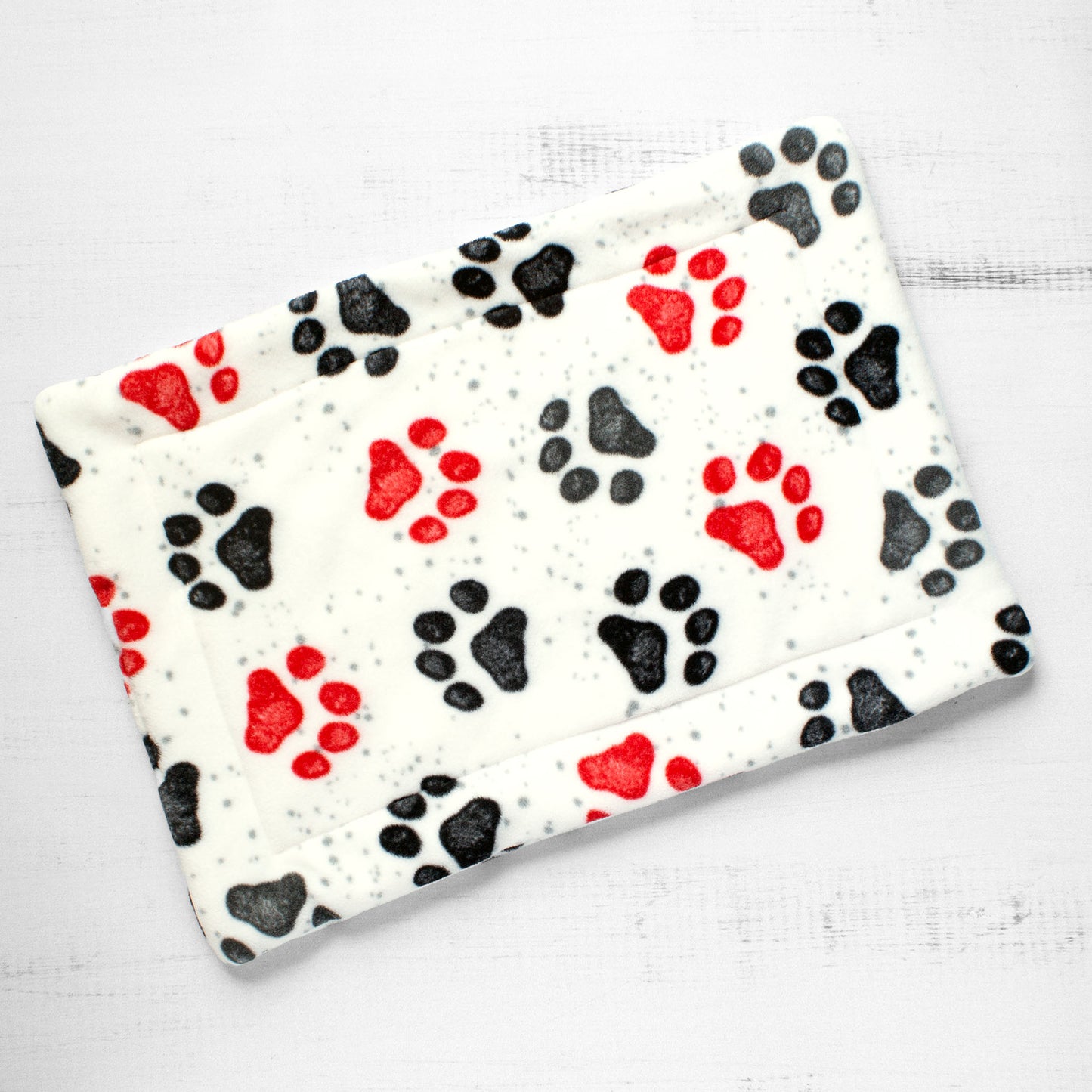 Top view of cat mat with red and black paw prints on whitish background.