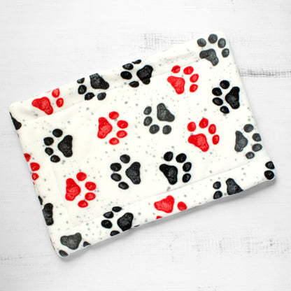 Top view of cat mat with red and black paw prints on whitish background.