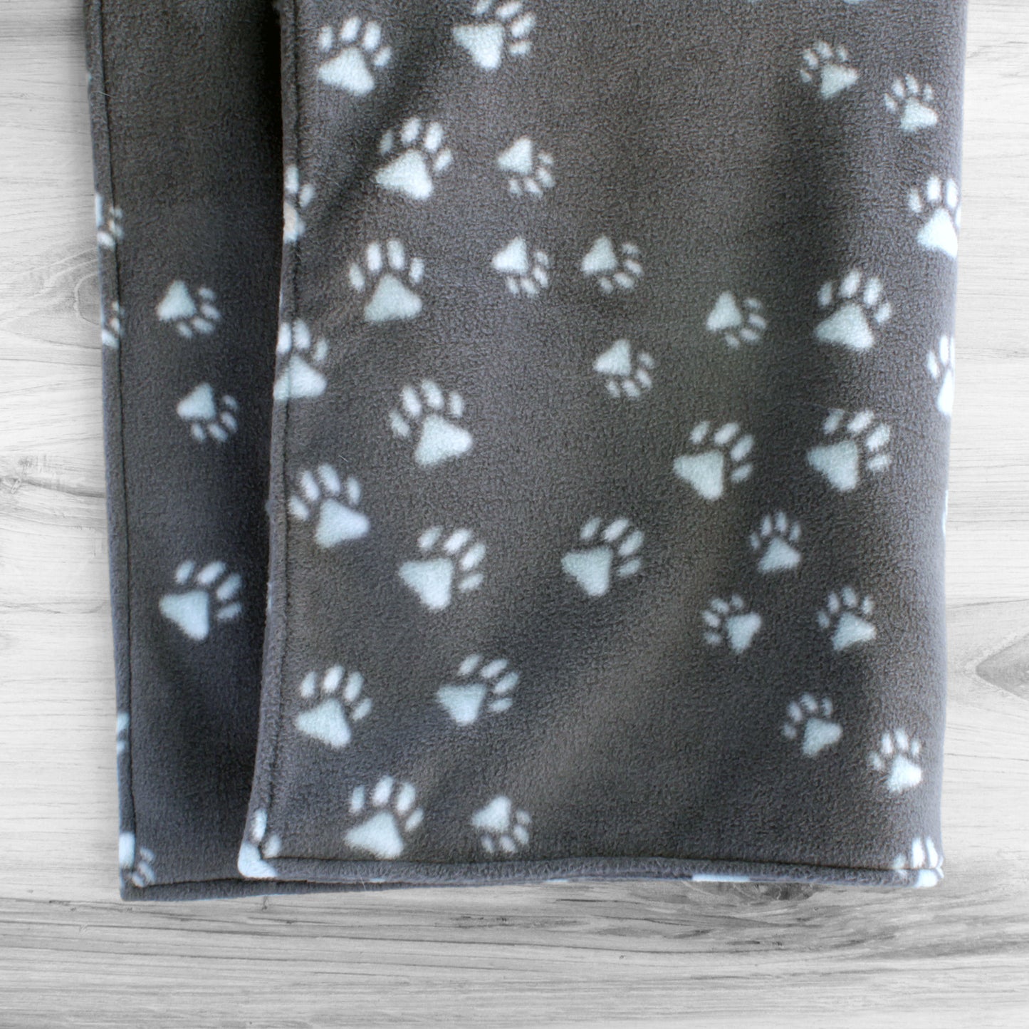 Dog blanket hanging up showing both sides with grey background and lightly tinted blue paw prints.