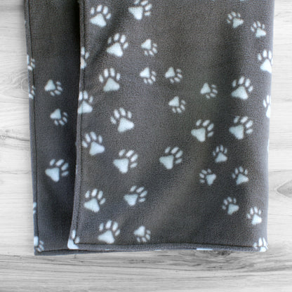 Dog blanket hanging up showing both sides with grey background and lightly tinted blue paw prints.