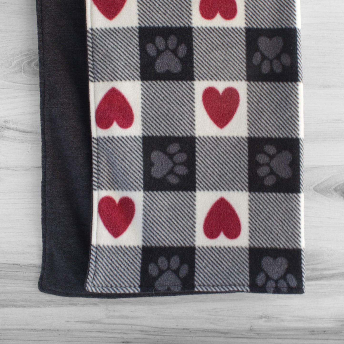 Dog blanket hanging up with red, white, and black squares. Some squared have red hearts and some have gray paws. Back side is solid dark heather grey.