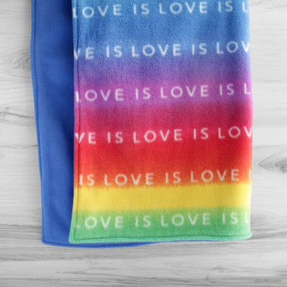 Dog blanket hanging up with the words Love Is Love repeated across front on a rainbow colored background. Back is turquoise color.