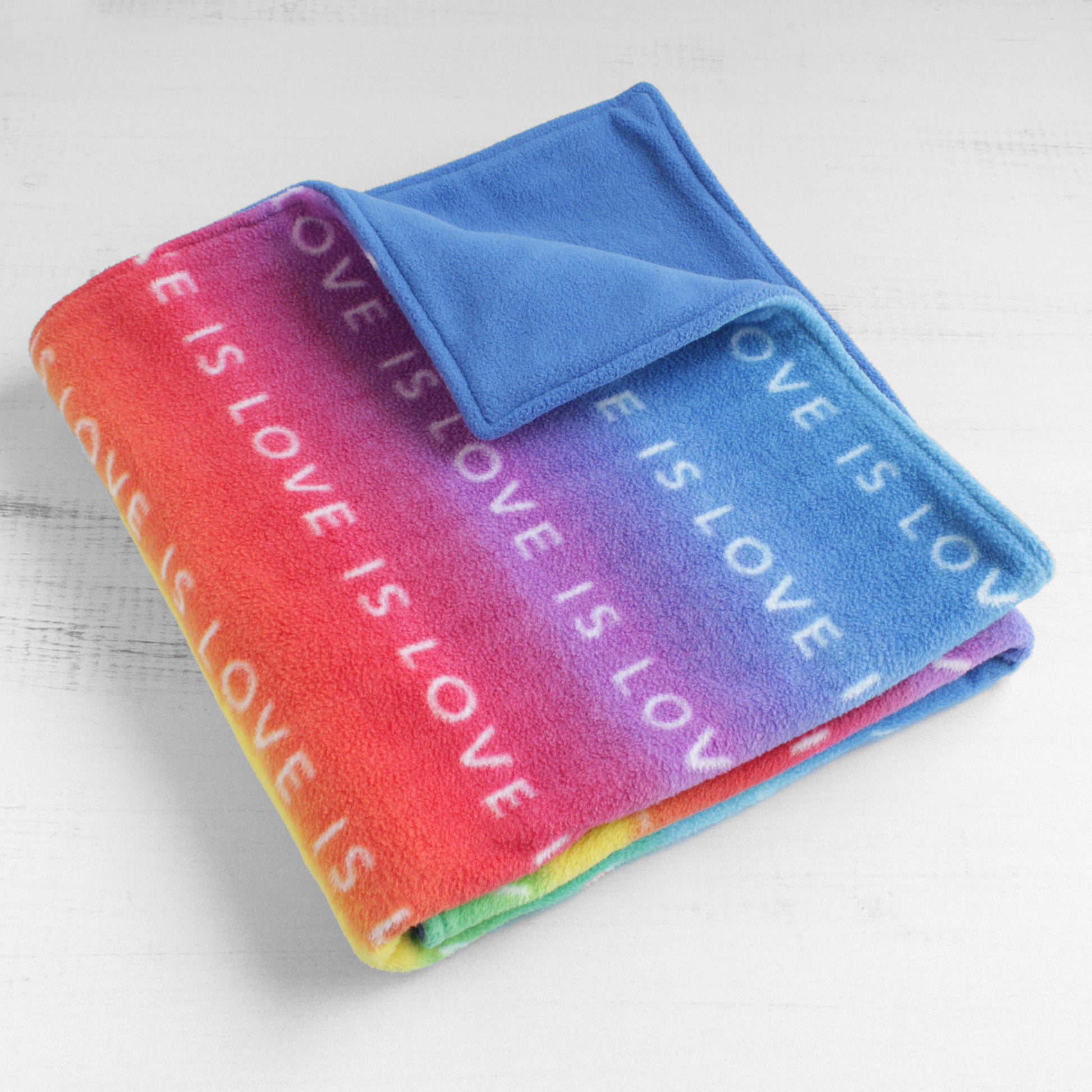 Dog blanket folded up with the words Love Is Love repeated across front on a rainbow colored background. Back is turquoise color.