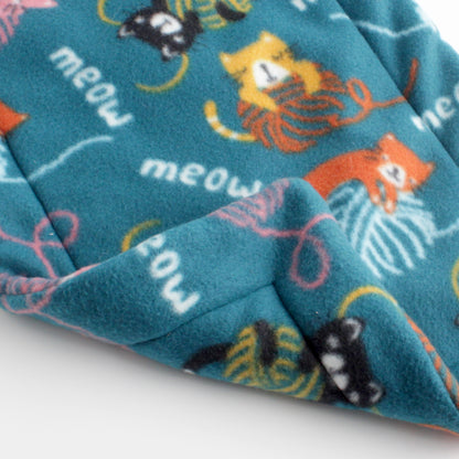 Closeup of cat mat with pattern of yellow, orange, pink, and black cats playing with balls of yard on a dark turquoise background. The back side is the same pattern.