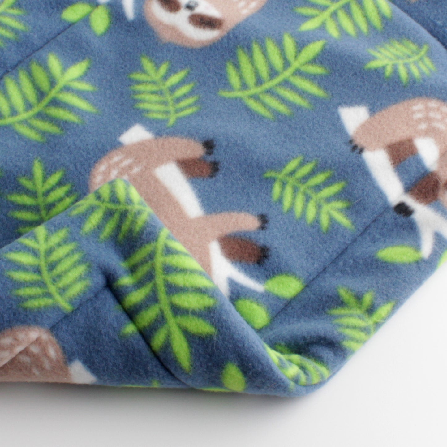 Closeup of cat mat showing the same cute sloth and leaves print on the front and back sides.